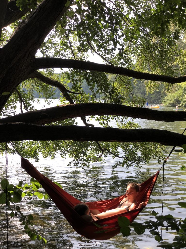 Gir reading a book in a red hammock hanging over the lake