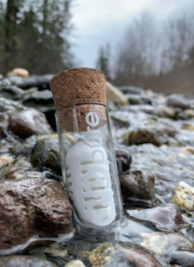 Glass jar with a white plastic water filter set in nature on the rocks near a waterfall