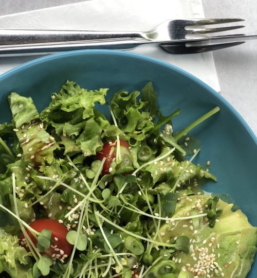 Green arugula salad lightly tossed dressing in a bowl with silver eating utensils